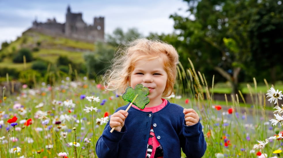 Cute toddler girl with Irish cloverleaf lollipop in a field of wild flowers